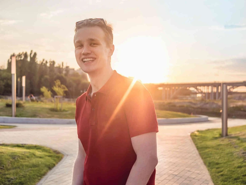 Junger Mann steht drau&szlig;en l&auml;chelend, sonne hinter ihm